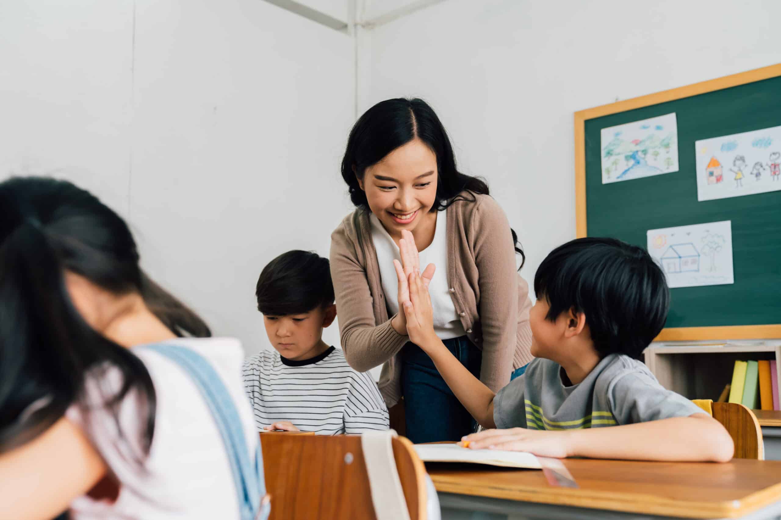 Woman teacher in classroom high fiving a student
